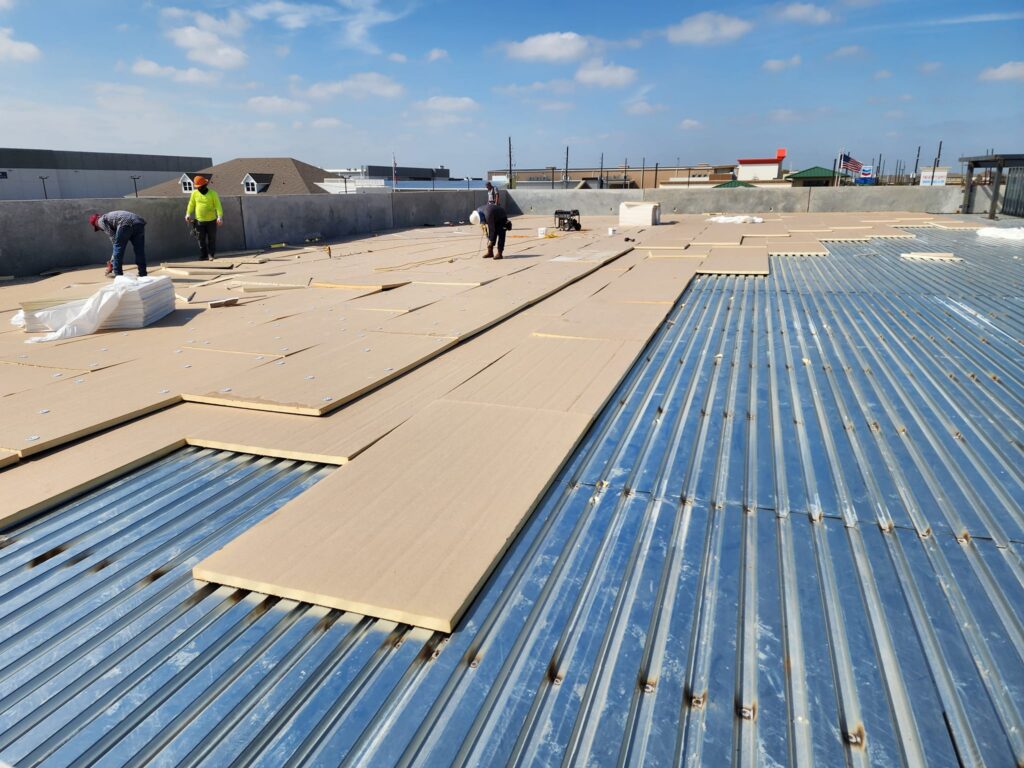 Construction workers installing insulation boards on a metal rooftop.