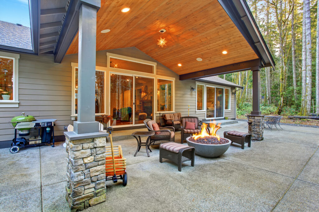 Cozy patio with outdoor fire pit and seating at modern home in forest setting.
