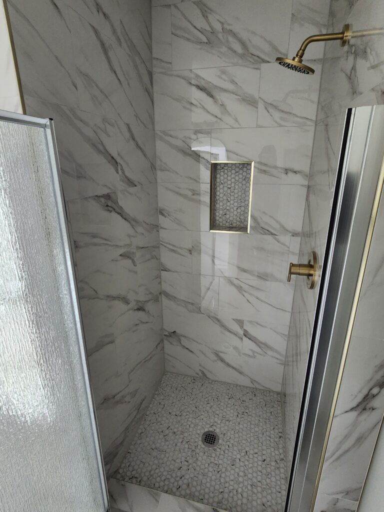 Modern marble-tiled shower stall with pebble floor and glass door.